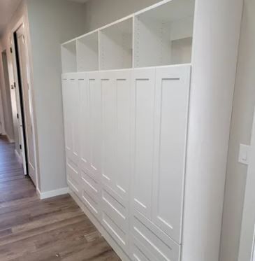 A hallway with a row of white cabinets and drawers.