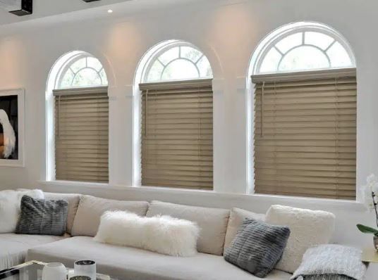 A living room with a couch and three arched windows with blinds.