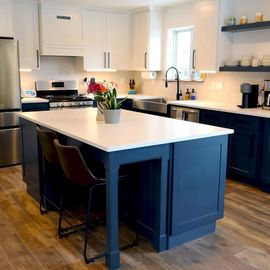 Bright modern kitchen with white cabinets, dark blue island, and a small plant centerpiece