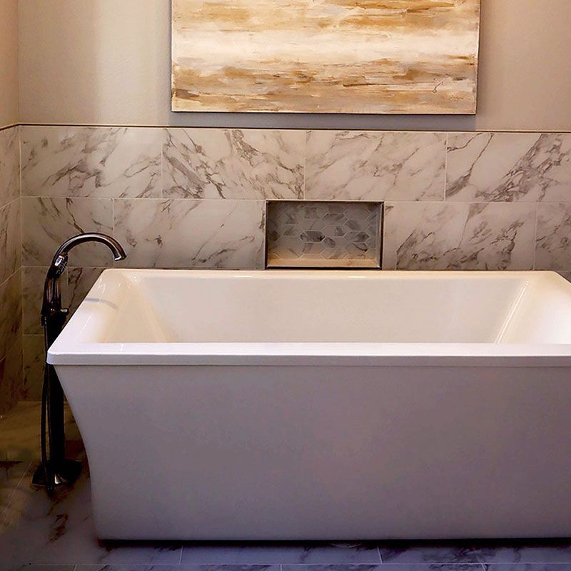 Modern bathroom with a white freestanding tub, black faucet, marble wall, and tan artwork above.