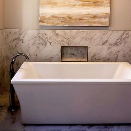 Modern bathroom with a white freestanding tub, black faucet, marble wall, and tan artwork above.