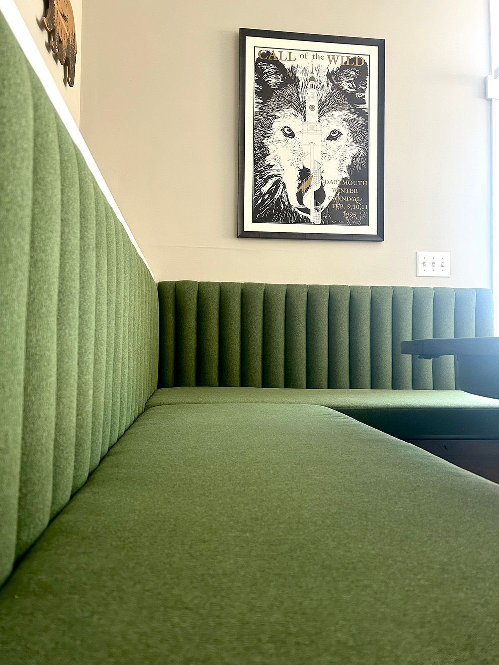 Green upholstered booth seat in a bright room, with a framed black-and-white artwork on the wall.