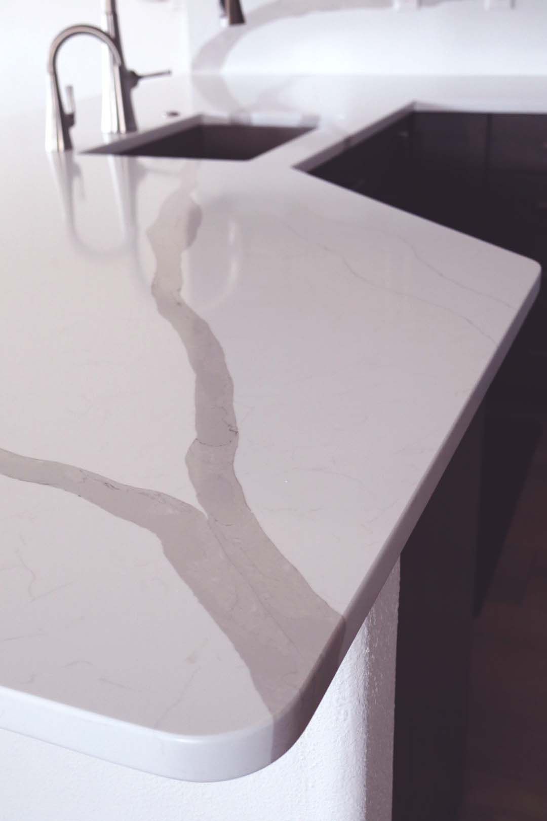 White kitchen countertop with gray marble veining and a sink in the background.