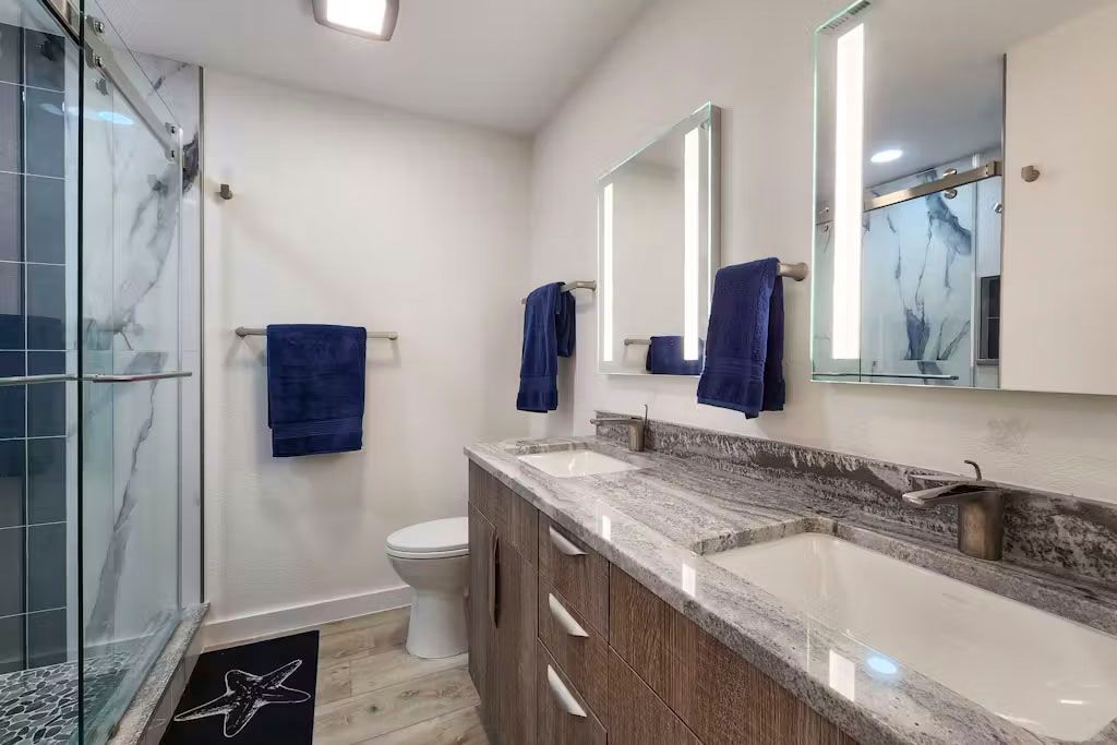 A bathroom with two sinks , a toilet , and a walk in shower.