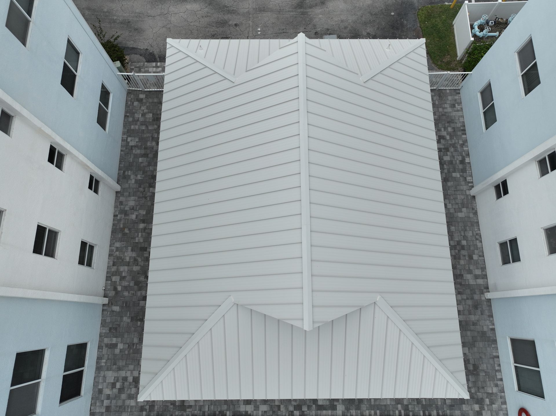 Overhead view of a building with a white roof and two light blue buildings flanking it.