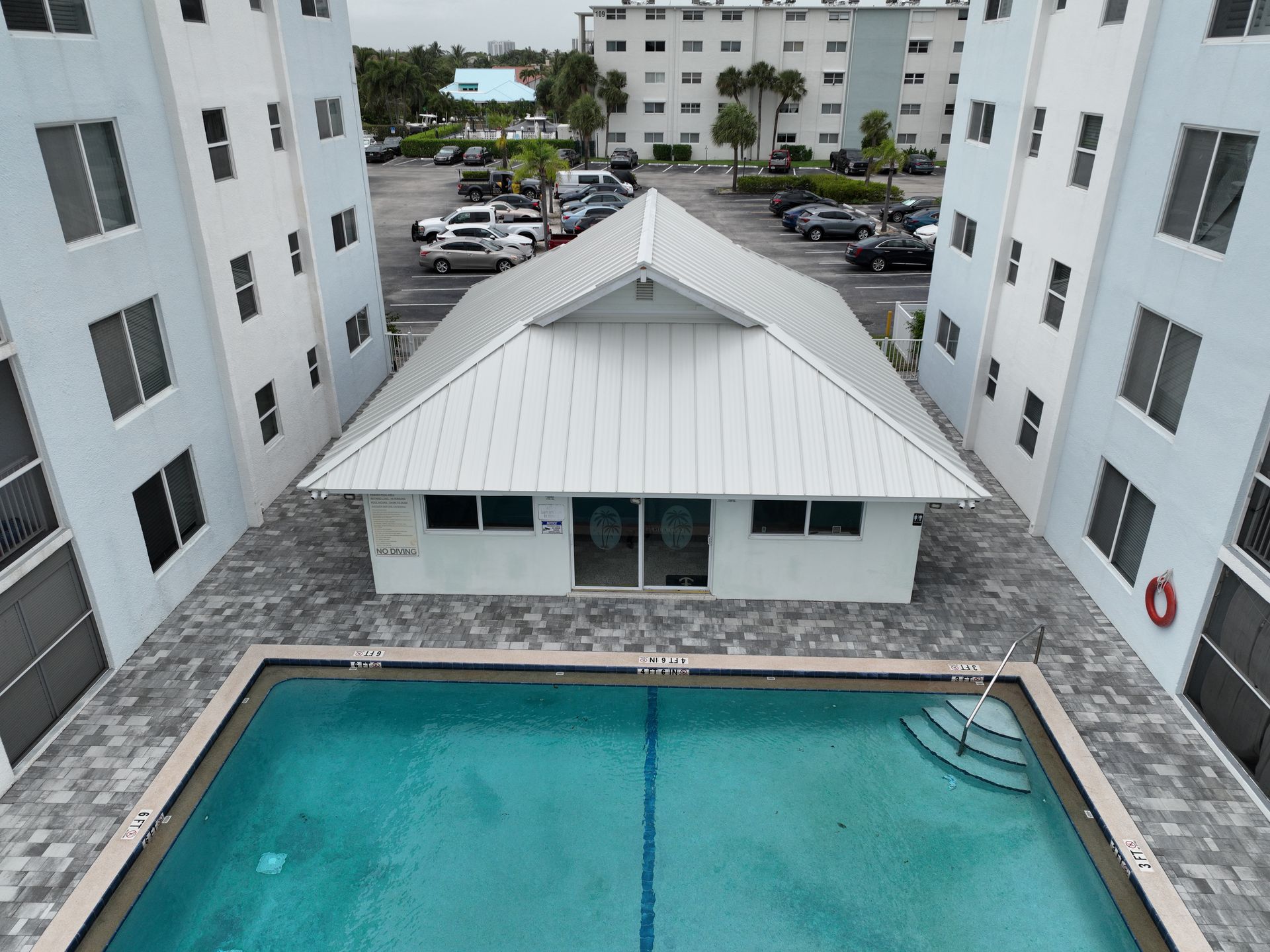 Pool between white apartment buildings; small white building with a gable roof.