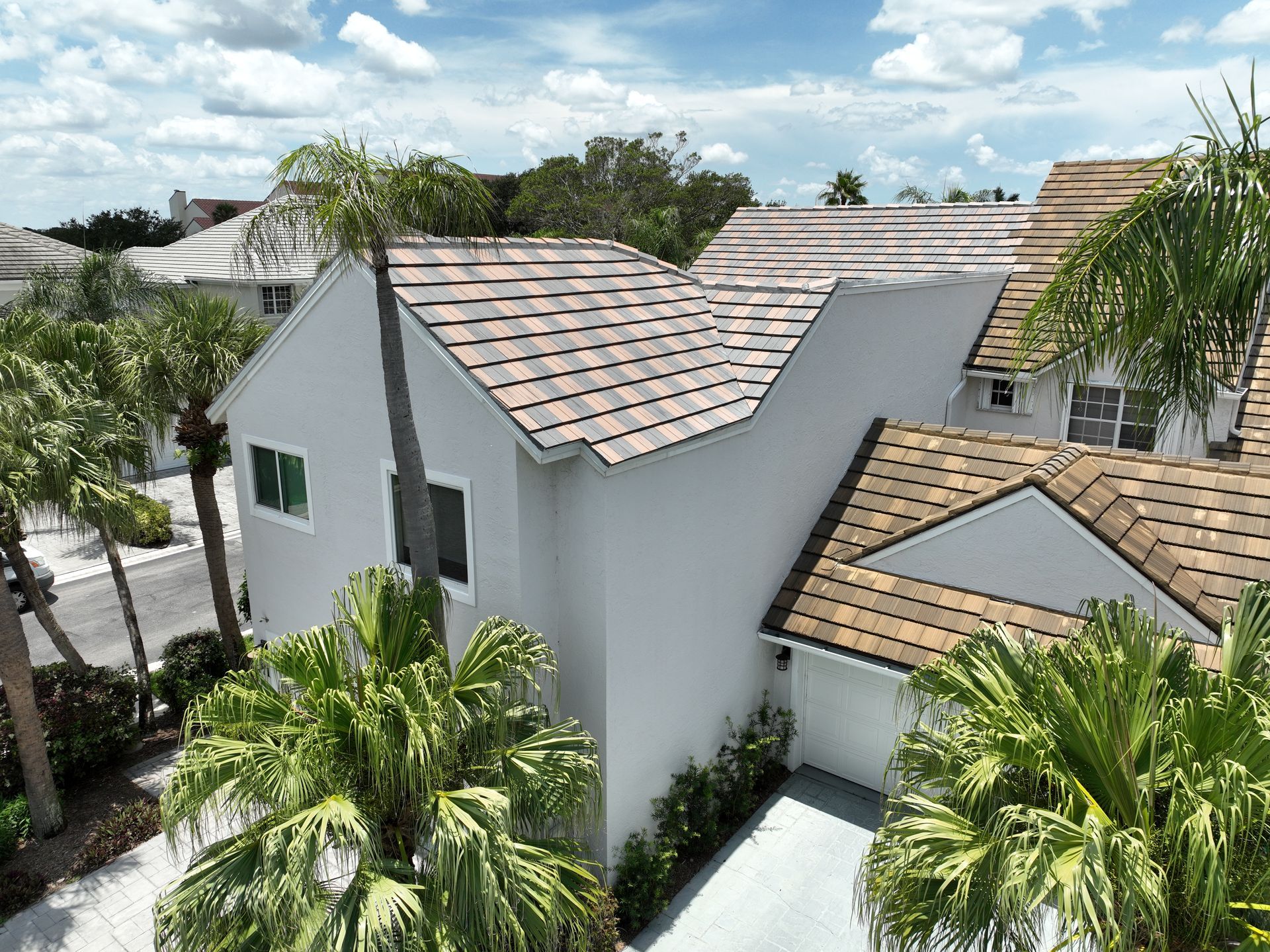 White house with brown tile roof surrounded by palm trees. Blue sky.