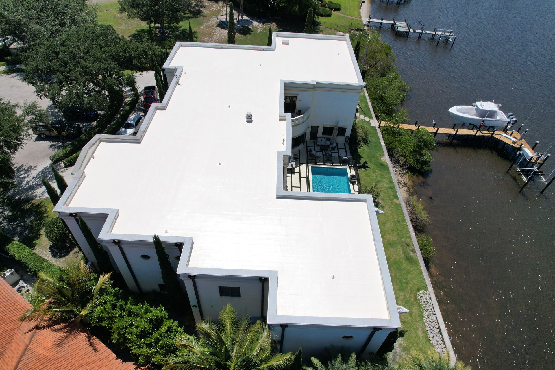 Aerial view of a modern white house with a flat roof, pool, dock, and water access.
