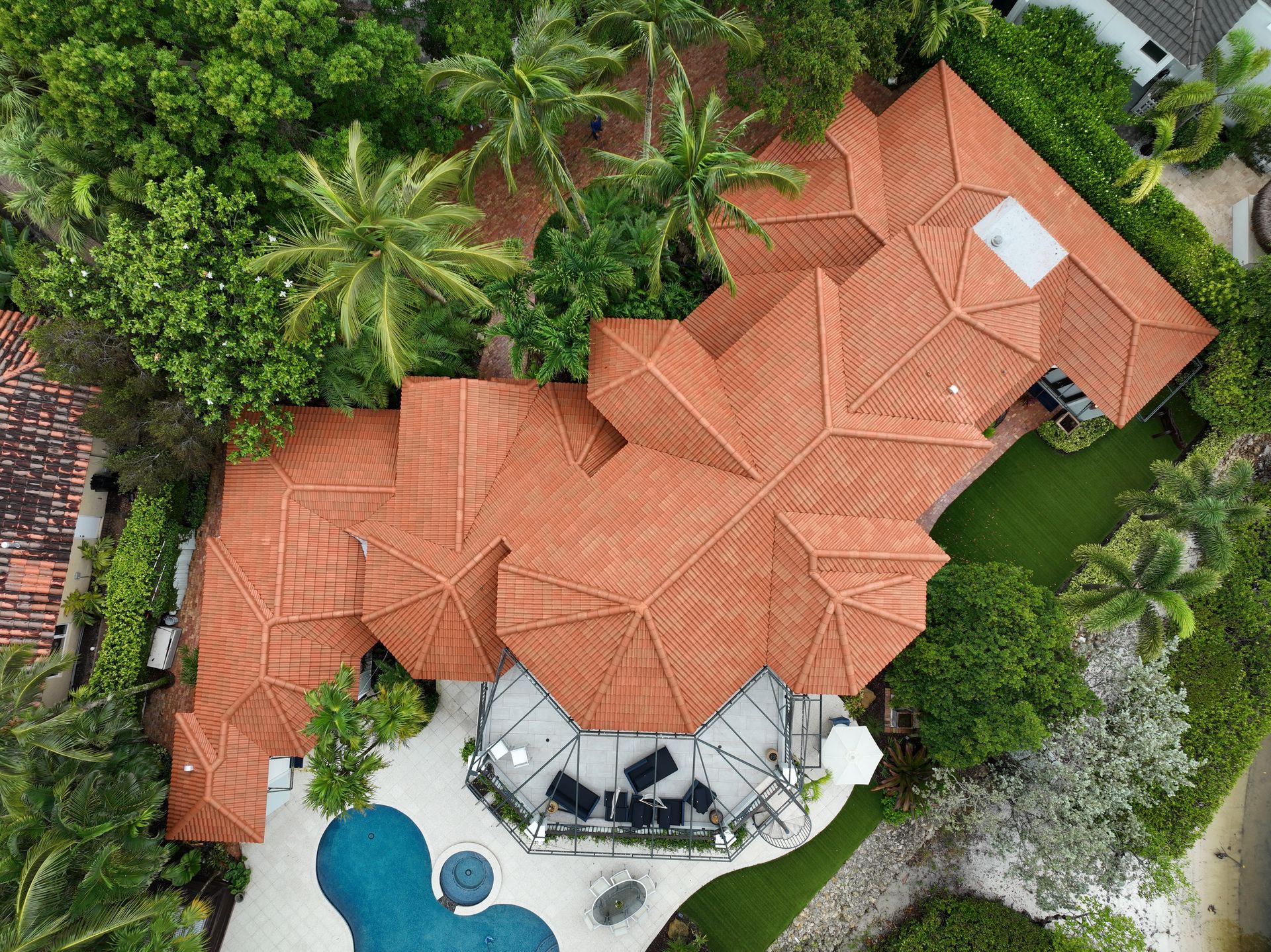 Aerial view of a house with terracotta roof, swimming pool, lush greenery, and outdoor seating area.