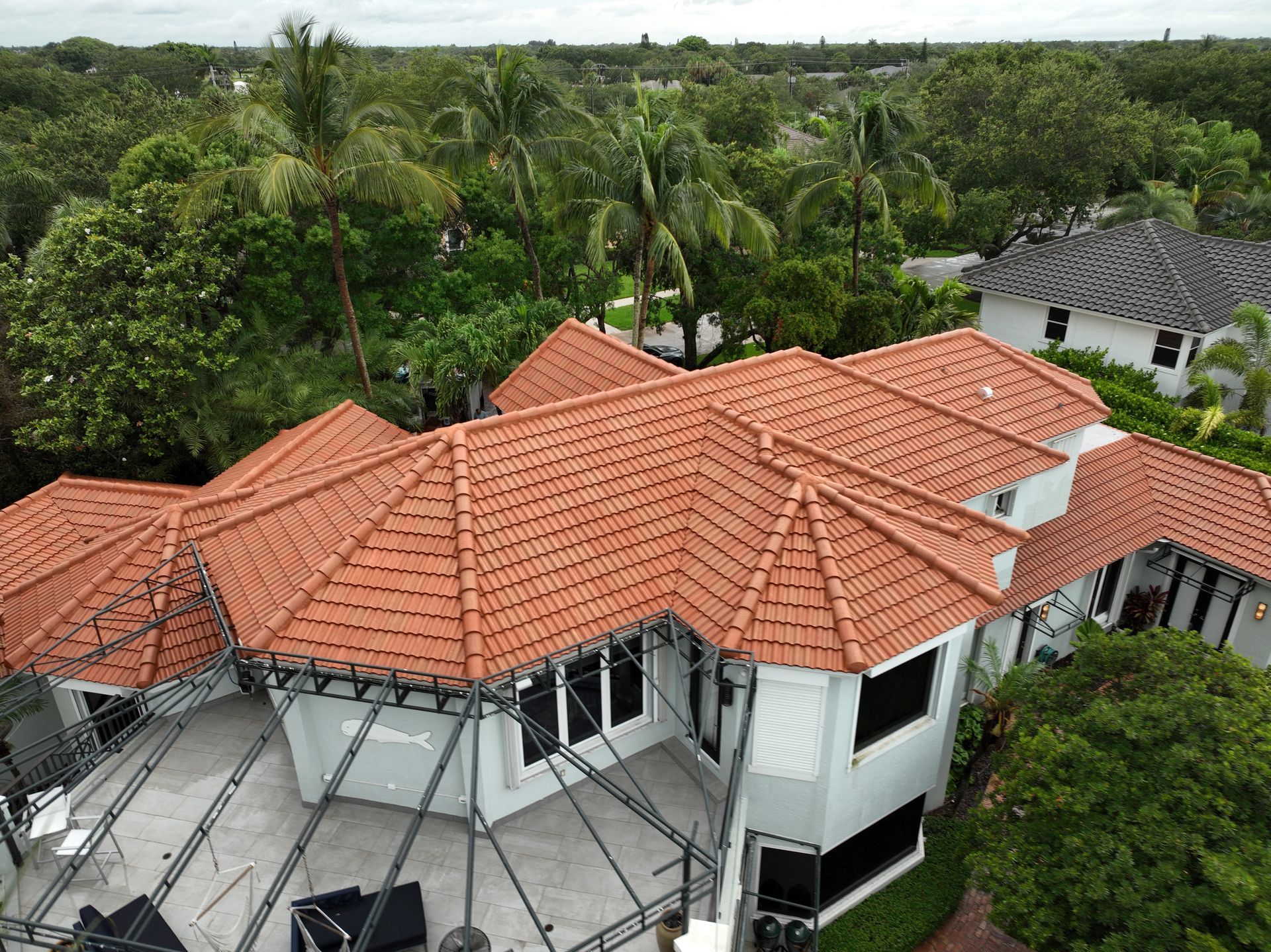 Aerial view of a house with an orange-tiled roof surrounded by green trees and a grey paved patio.