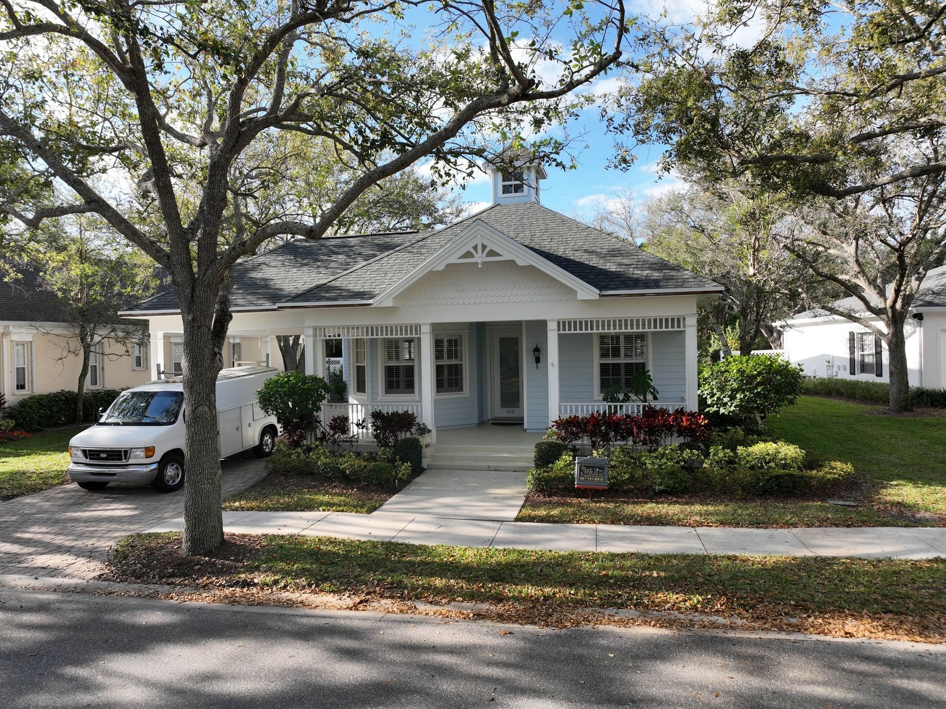 Light blue cottage with white trim and a small front porch; a van is parked in the driveway.