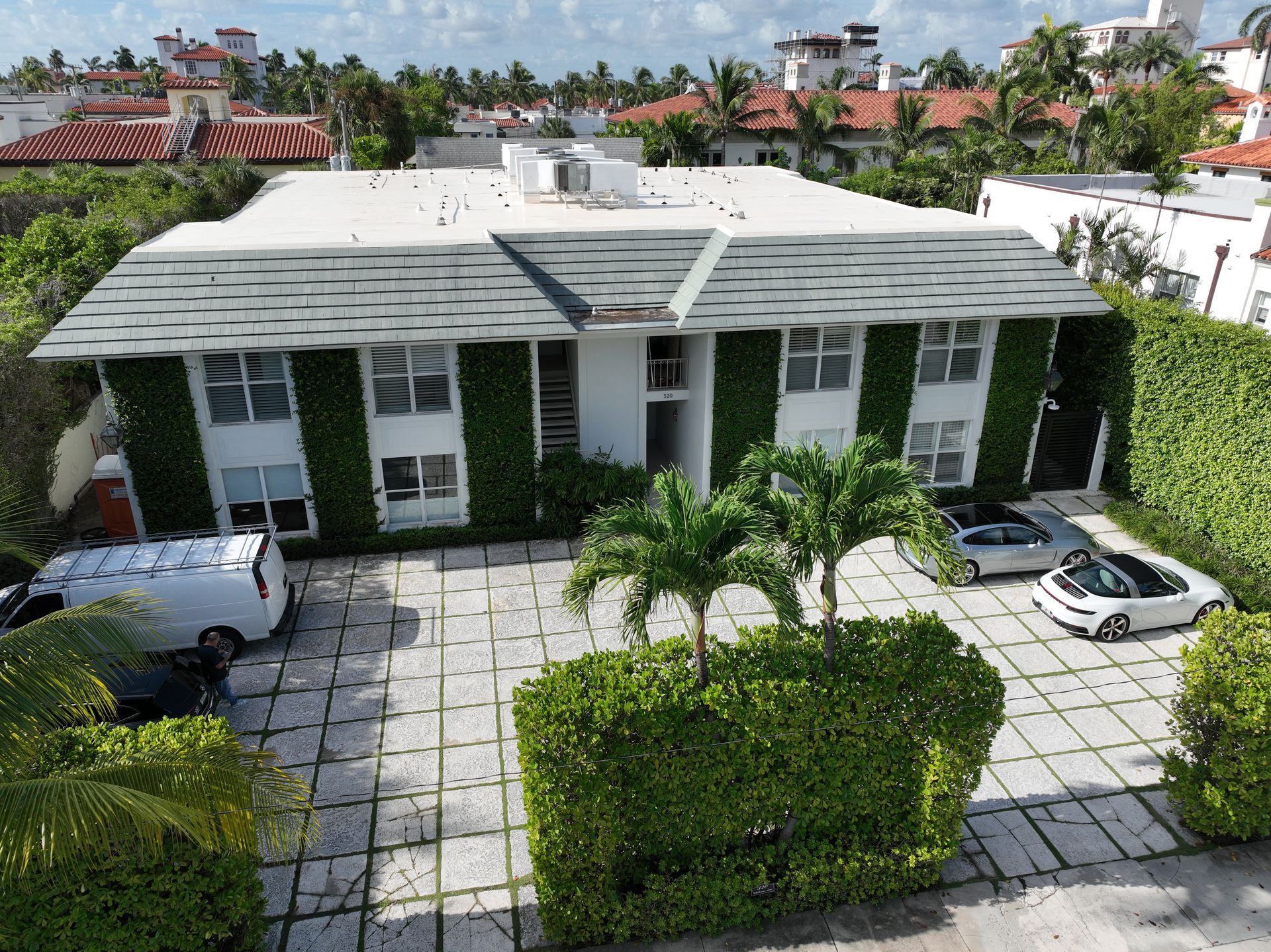 Two-story white building with green ivy, palm trees, and parked cars in a sunny area.