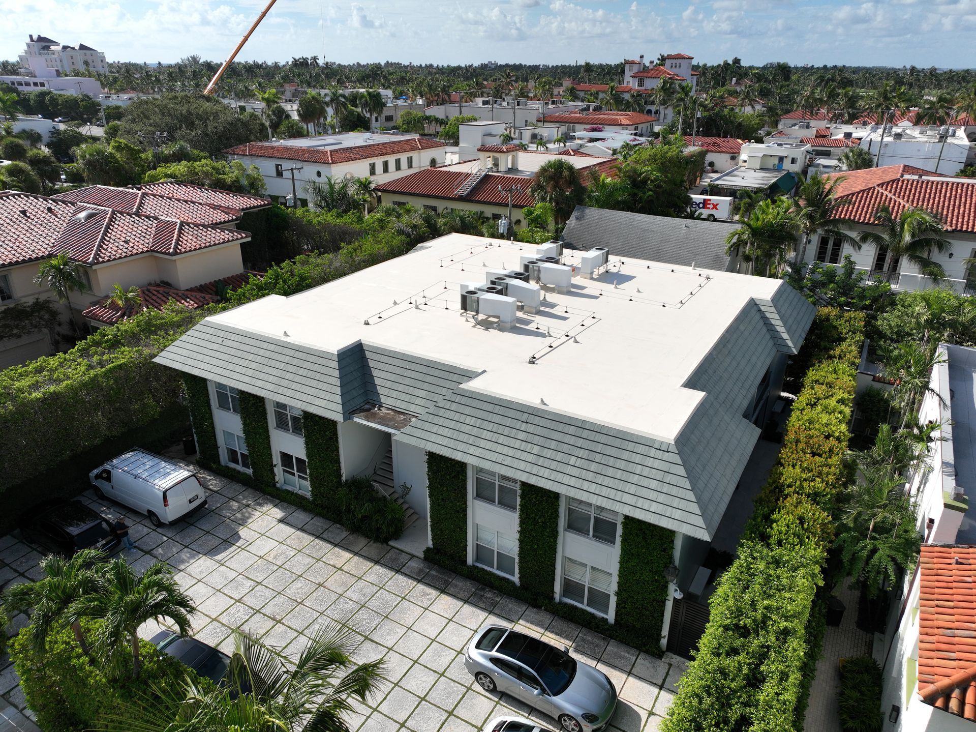 Aerial view of a white multi-story building with green ivy, a flat gray roof, and a paved driveway.