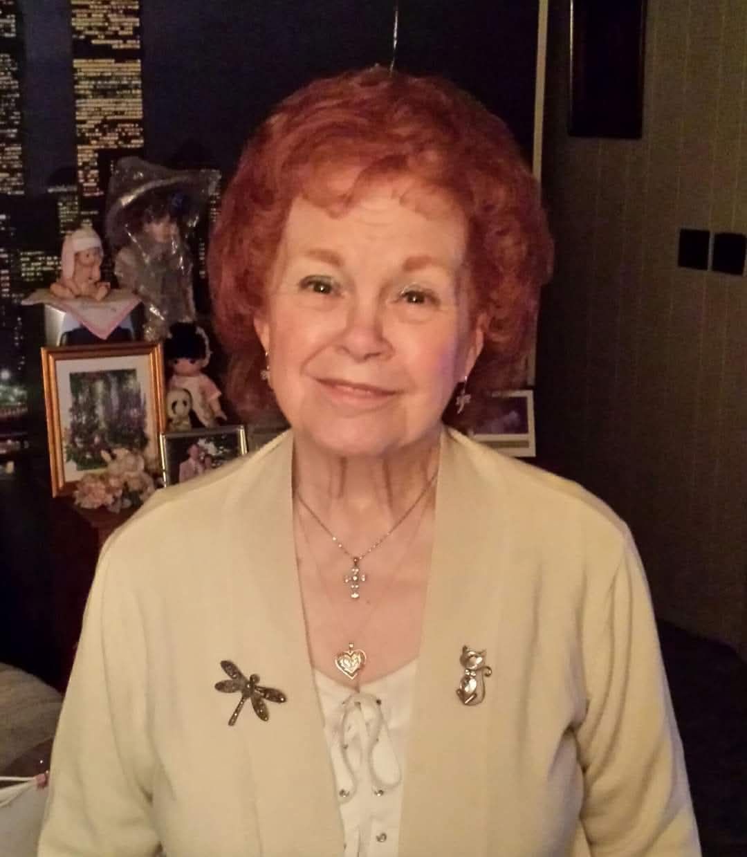 A woman with red hair is wearing a white jacket and a dragonfly brooch