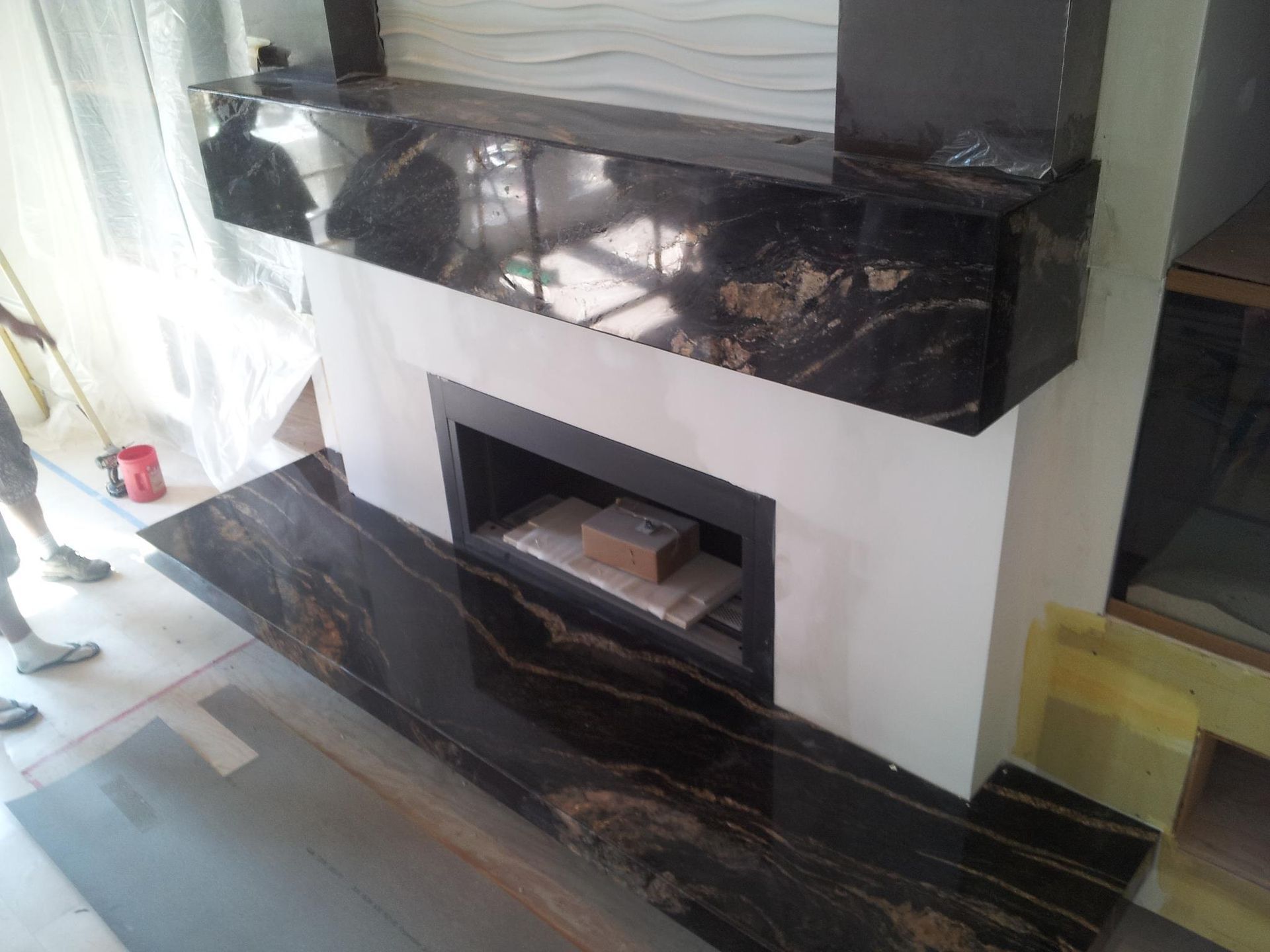 Fireplace with black granite surround and hearth; white wall, someone working.
