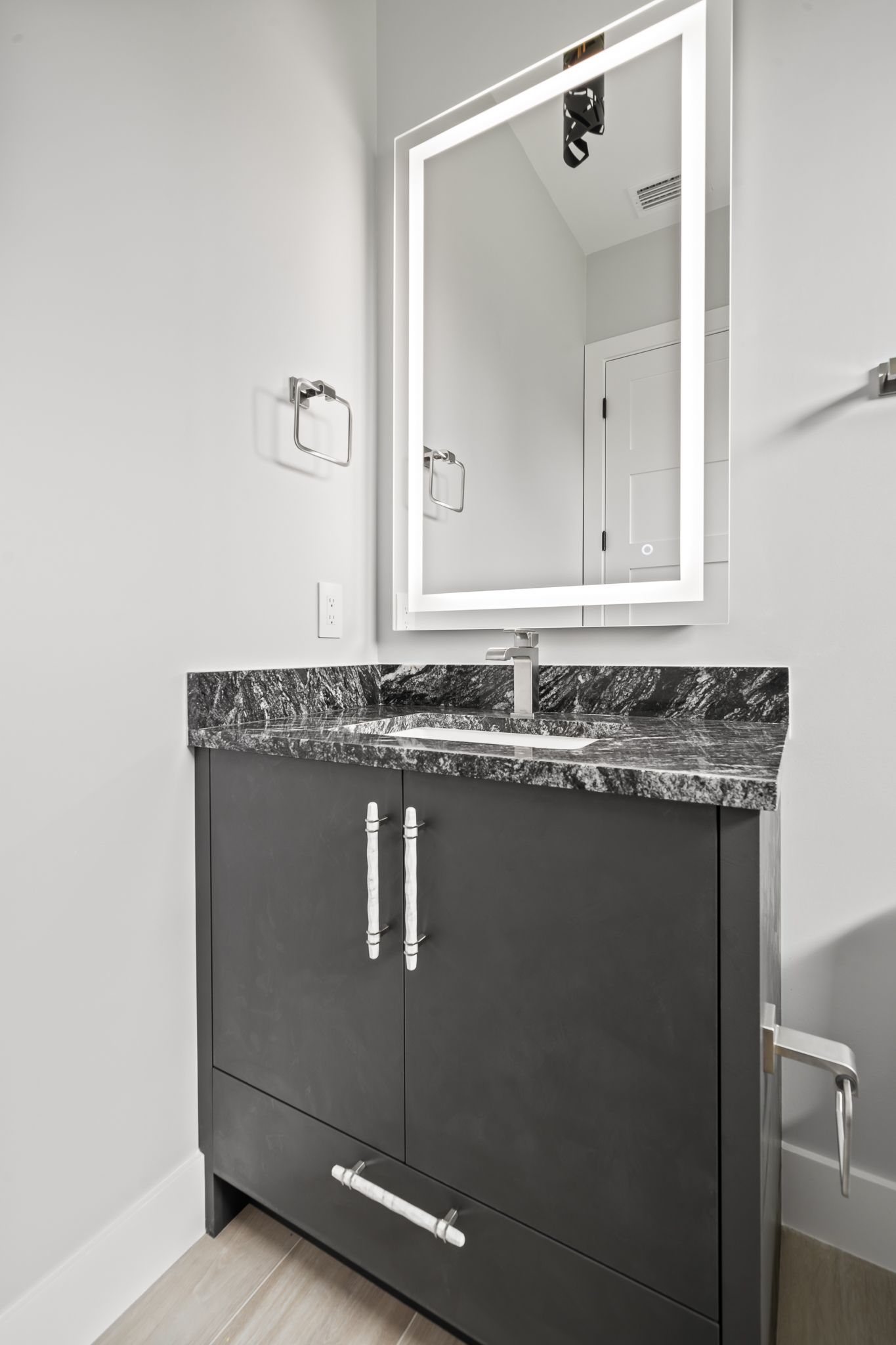 Dark gray bathroom vanity with granite countertop and a lighted mirror.