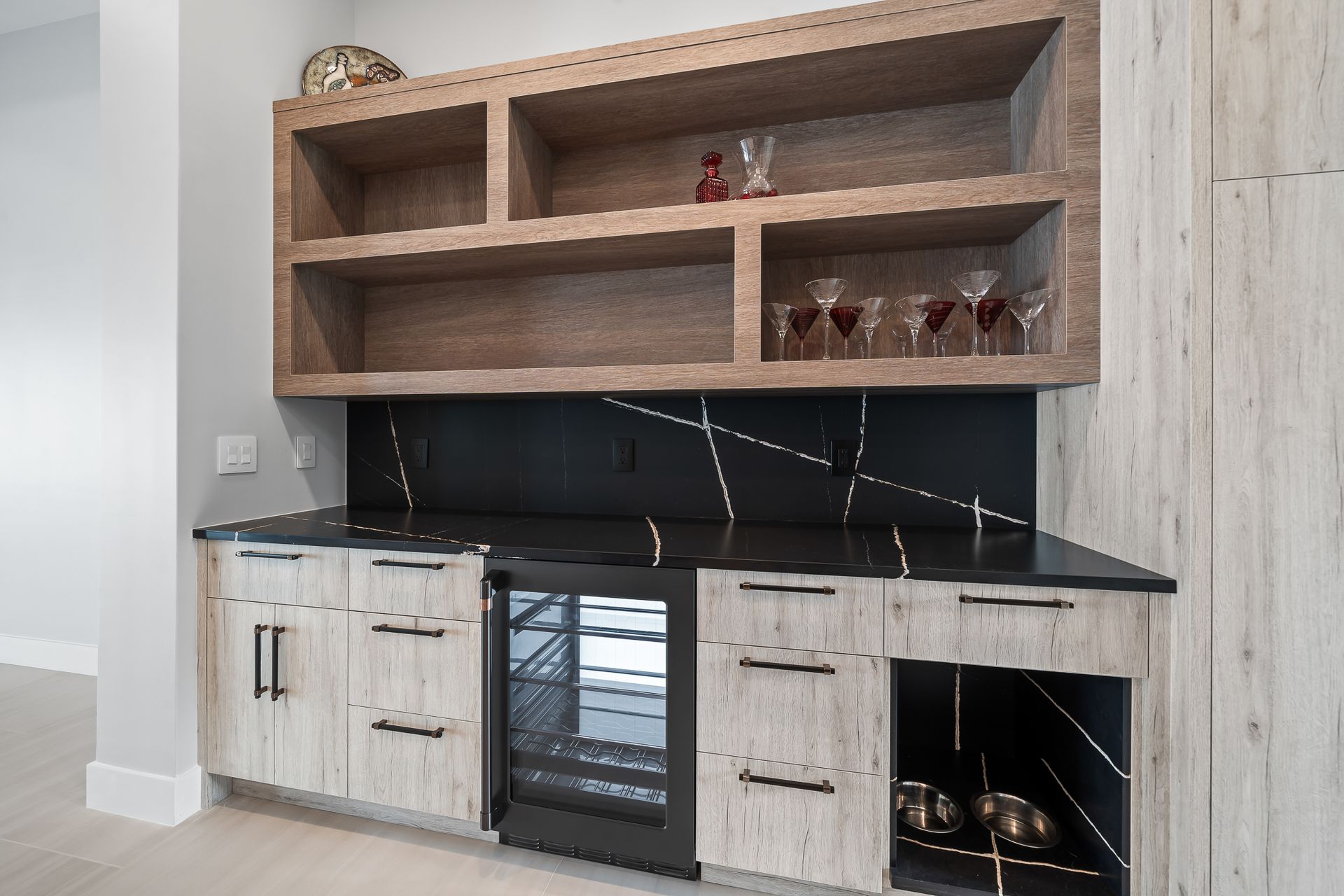Built-in home bar with wooden shelves, black countertop, wine fridge, and cabinets.