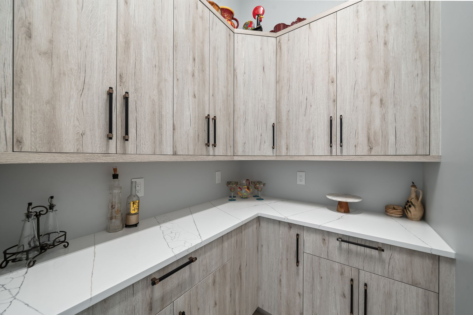 Corner pantry with light wood cabinets, white countertops, and black hardware.