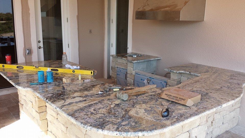 Outdoor kitchen under construction with granite countertop and stone facade.