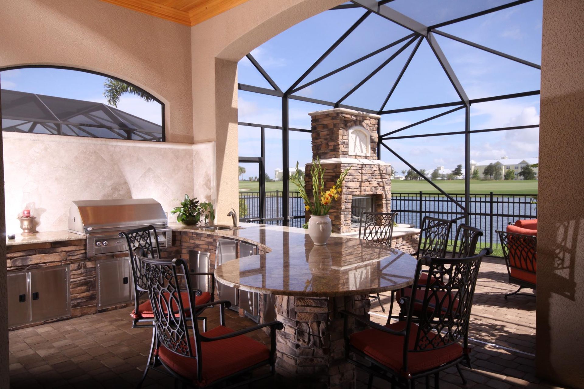 Outdoor kitchen with stone accents, built-in grill, and seating area overlooking a lake.