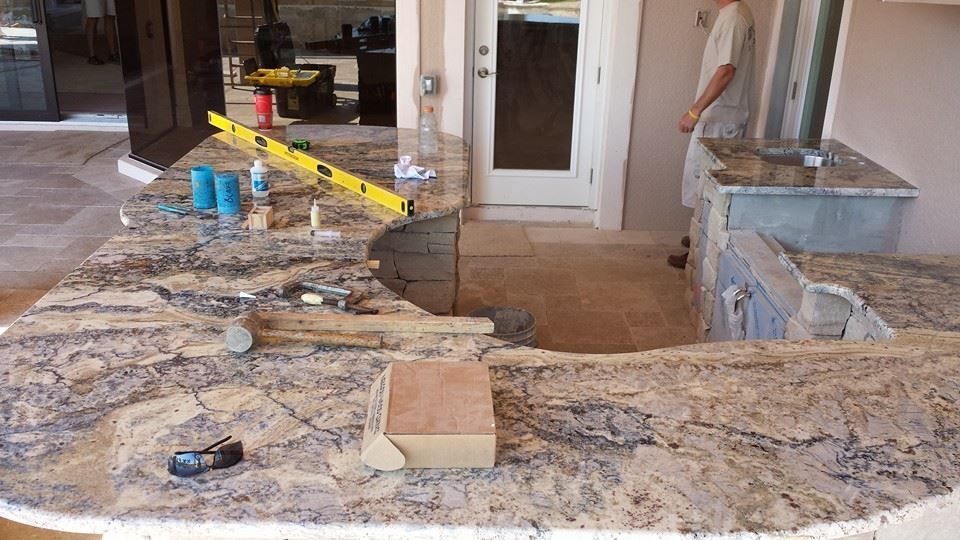 Granite countertop installation on a patio. Tools, materials, and a worker are present.