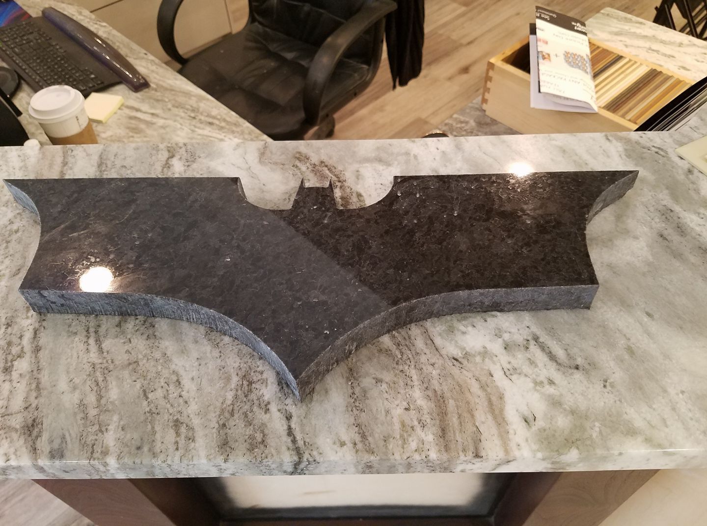 A Batman logo-shaped countertop of black granite on a light marble counter.