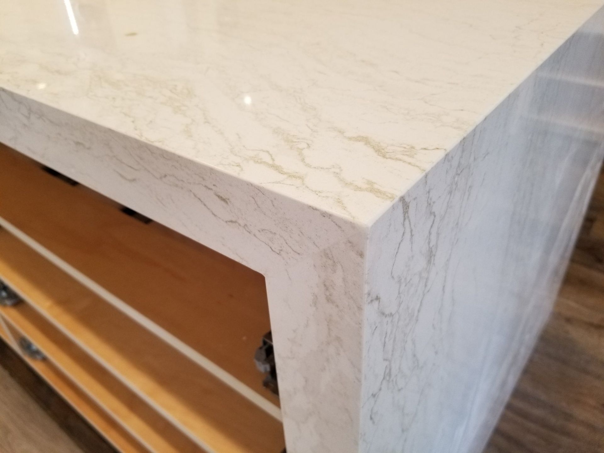 Light-colored countertop with subtle veining, on a wood cabinet. Corner in focus.
