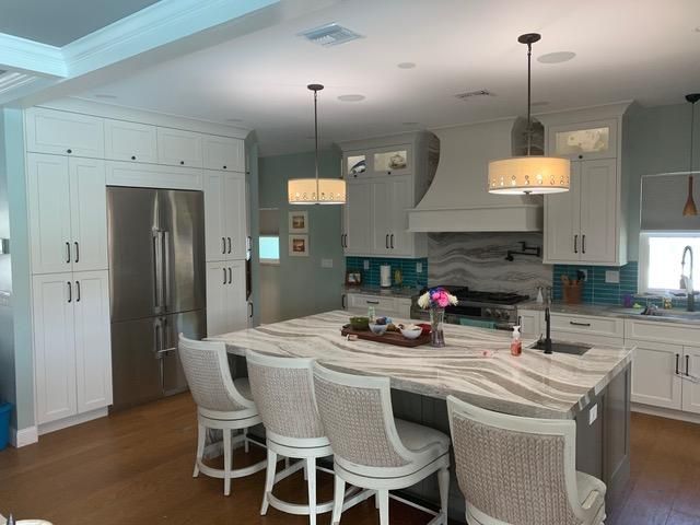 Elegant white kitchen with island, pendant lights, stainless steel appliances, and blue accents.