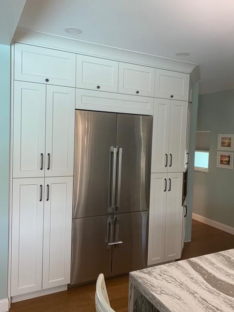 White kitchen cabinets surround a stainless steel refrigerator.