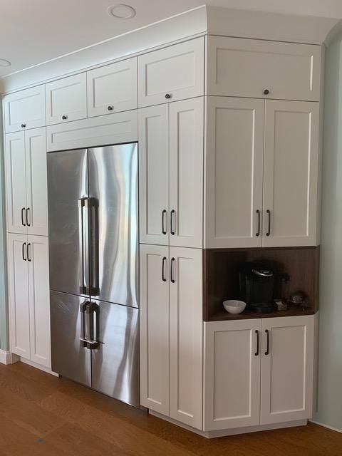 Built-in white cabinets surround a stainless steel refrigerator. A coffee station is included in the design.