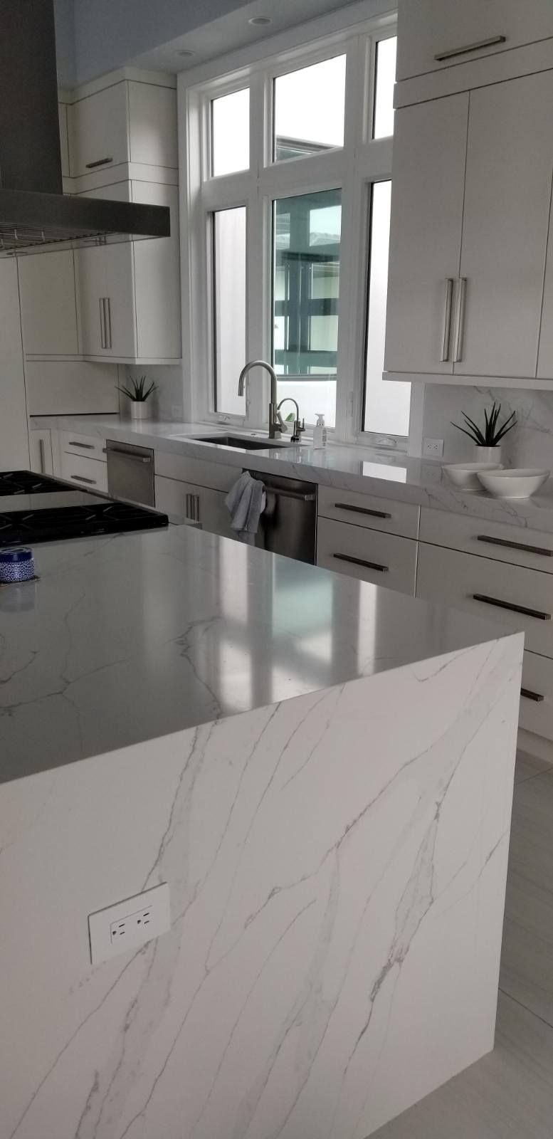 White kitchen with a large island and window, cabinets, and appliances.