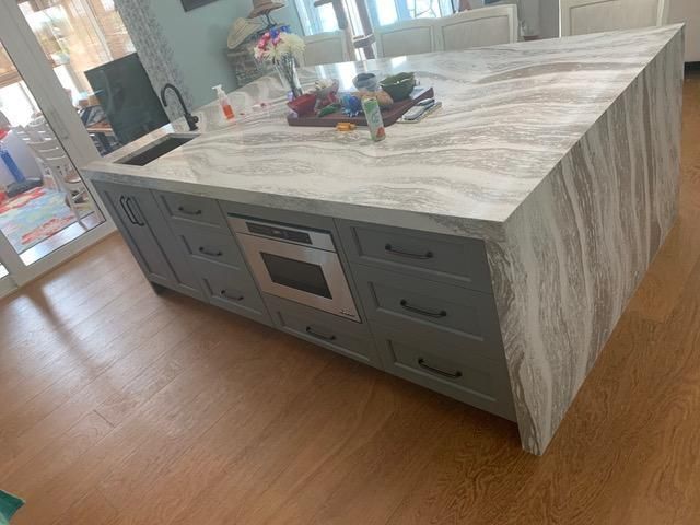 Kitchen island with gray cabinets, marble countertop, and built-in microwave.