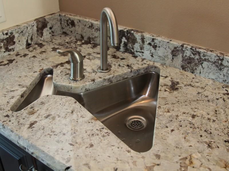 Stainless steel triangular sink with faucet in a granite countertop.