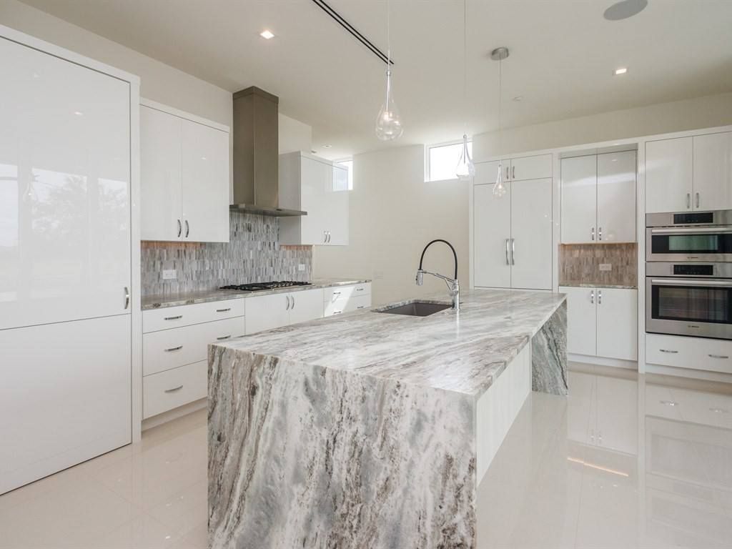 Modern white kitchen with a large marble island and stainless steel appliances.