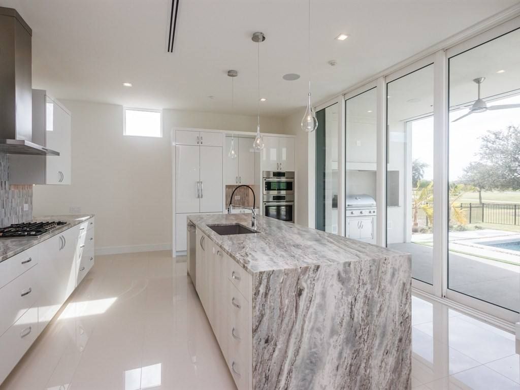 Modern white kitchen with large marble island and sliding glass doors to patio.