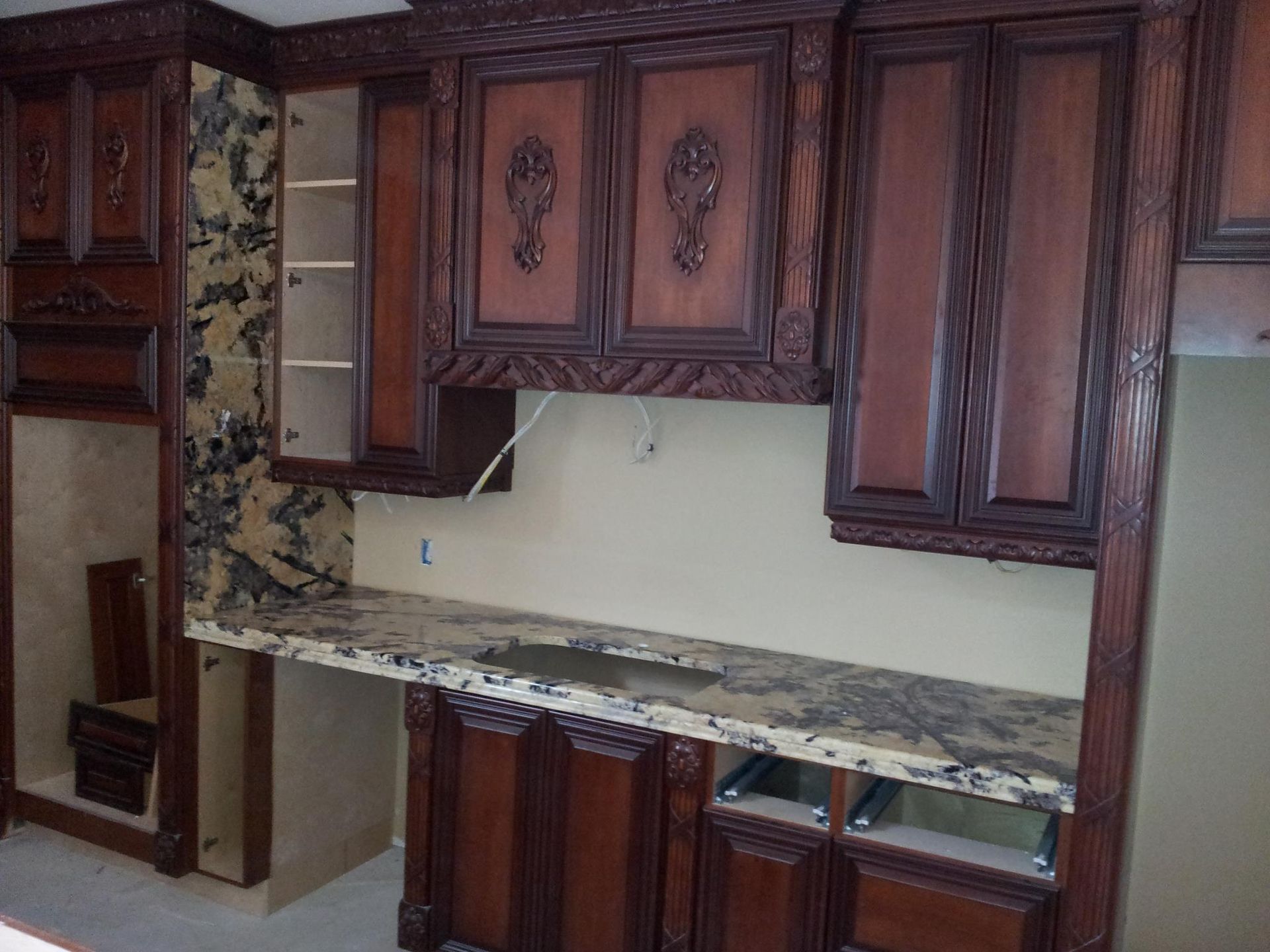 Kitchen cabinets with ornate dark wood detailing and granite countertops under construction.