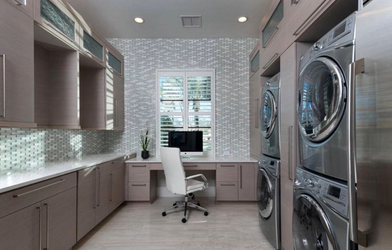 Laundry room with stacked washer and dryer, desk, and cabinets. Gray and white color scheme.