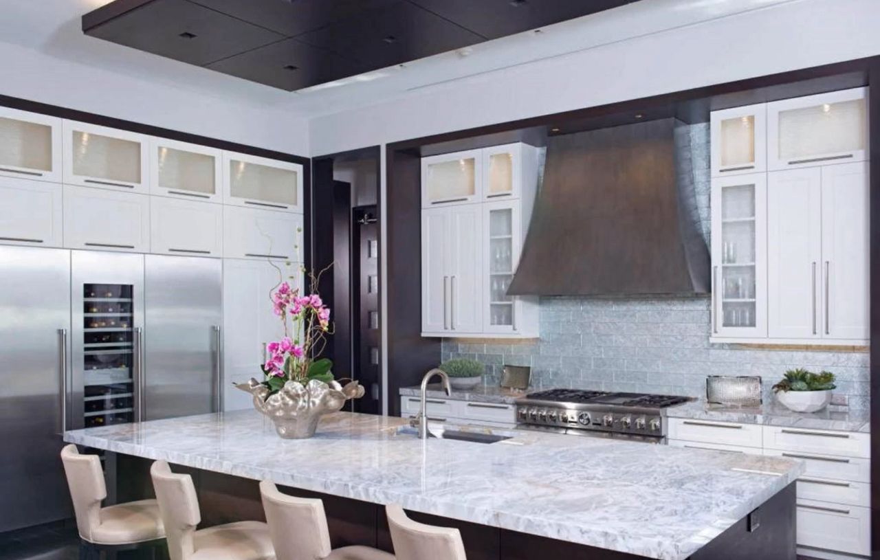 Modern kitchen with white cabinets, stainless steel appliances, and a large marble island.