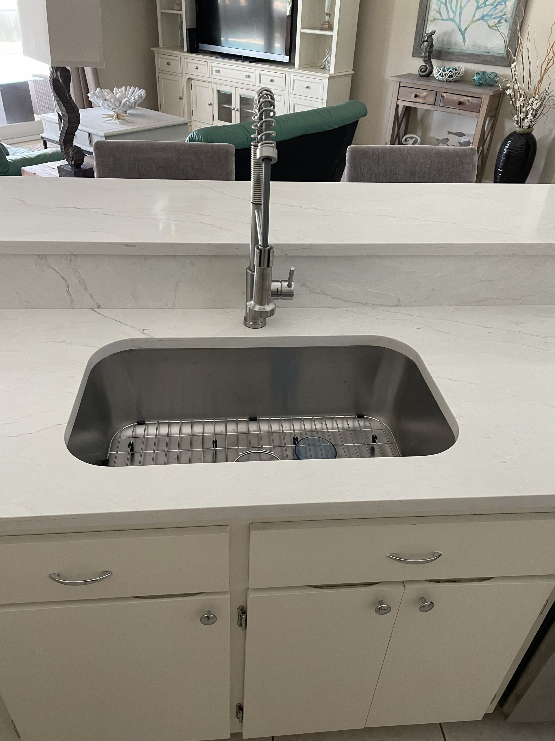 Stainless steel kitchen sink in white countertop, with silver faucet and cabinets.