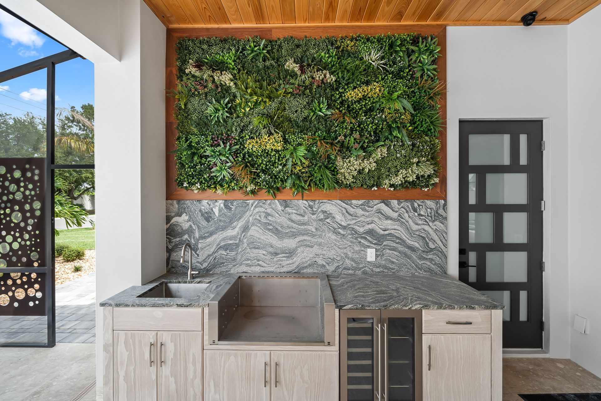 Outdoor kitchen with gray countertop, sink, grill, wine fridge, and a living wall.