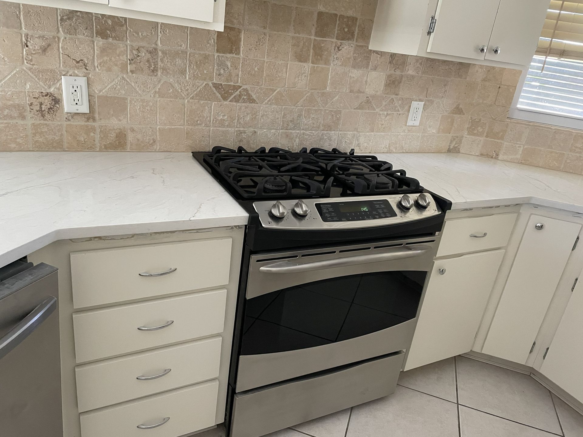 Kitchen with white countertops, stainless steel stove, cream cabinets, and tile backsplash.
