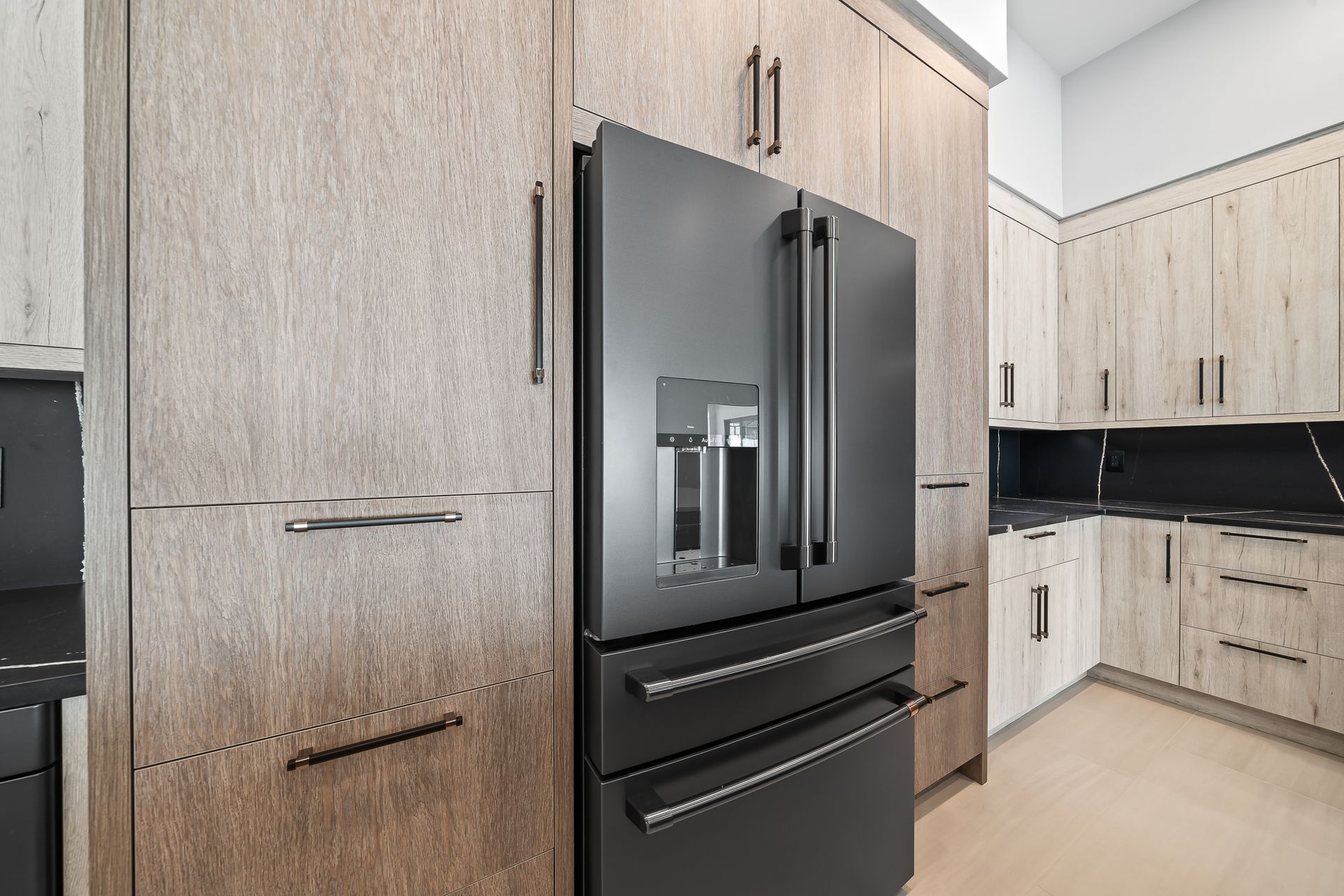Black refrigerator in a kitchen with light wood grain cabinets and a black countertop.