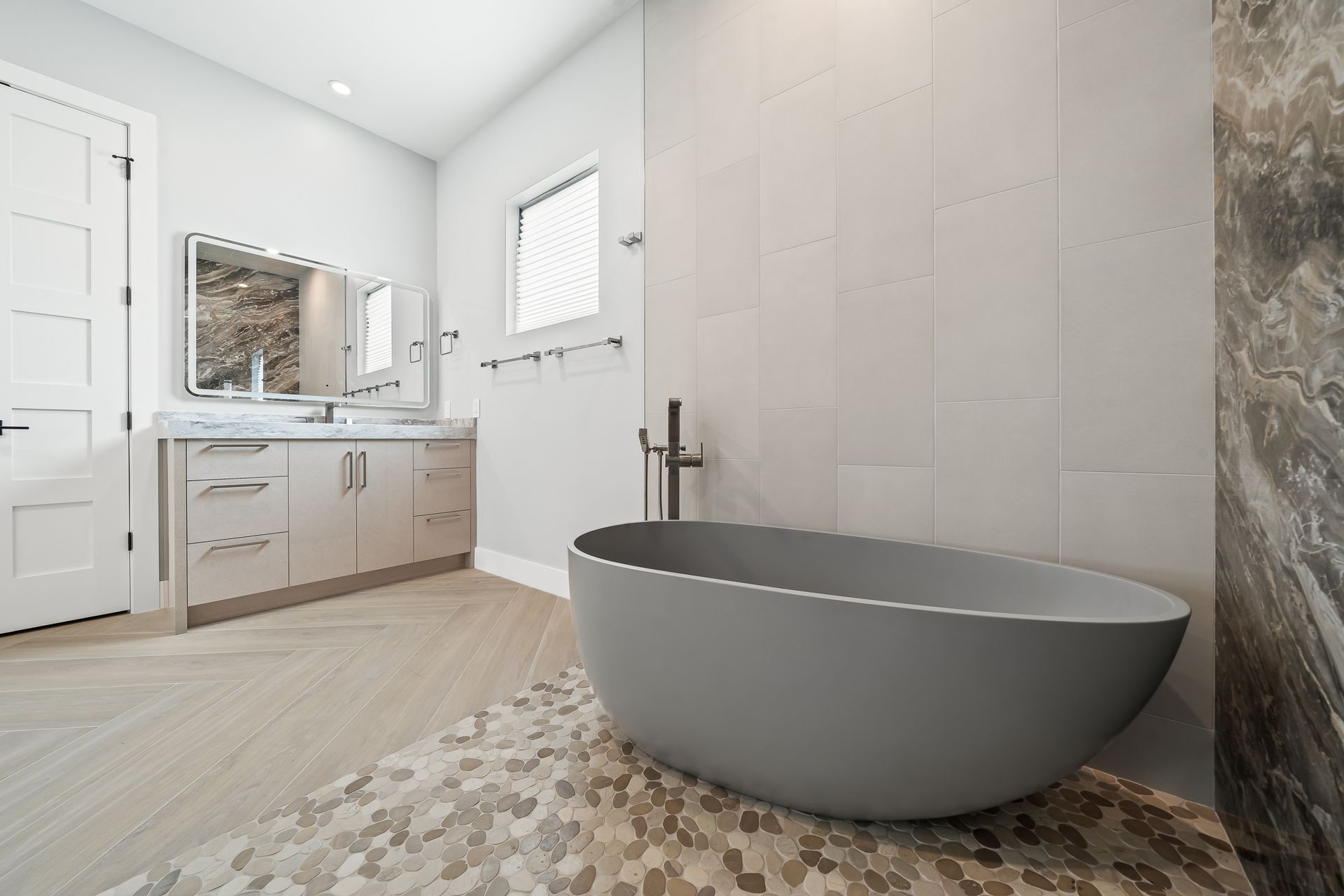 Modern bathroom with a gray soaking tub, vanity, and neutral tile.