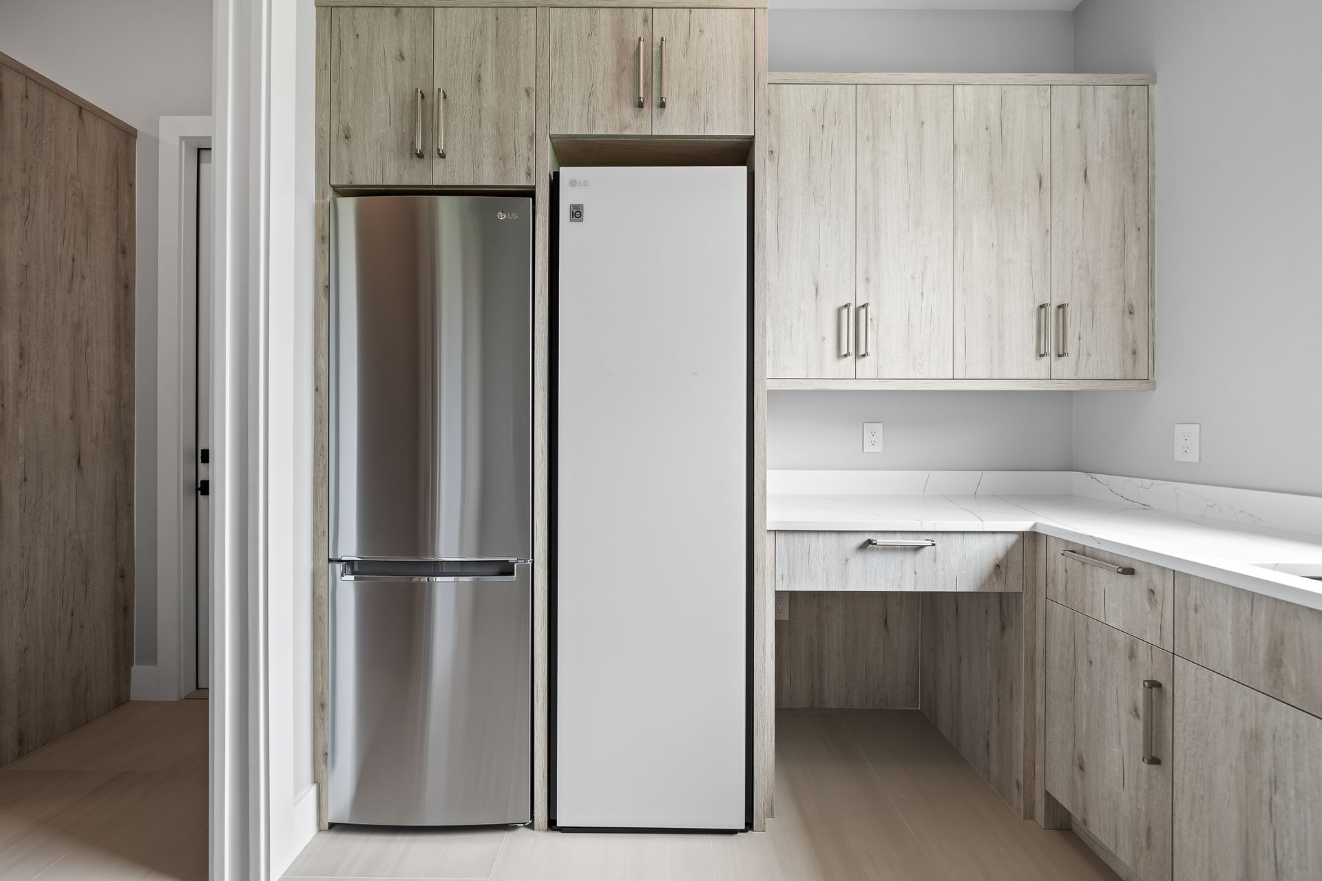 A kitchen with light wood grain cabinets, a stainless steel refrigerator, and a white refrigerator; also features a built-in desk.