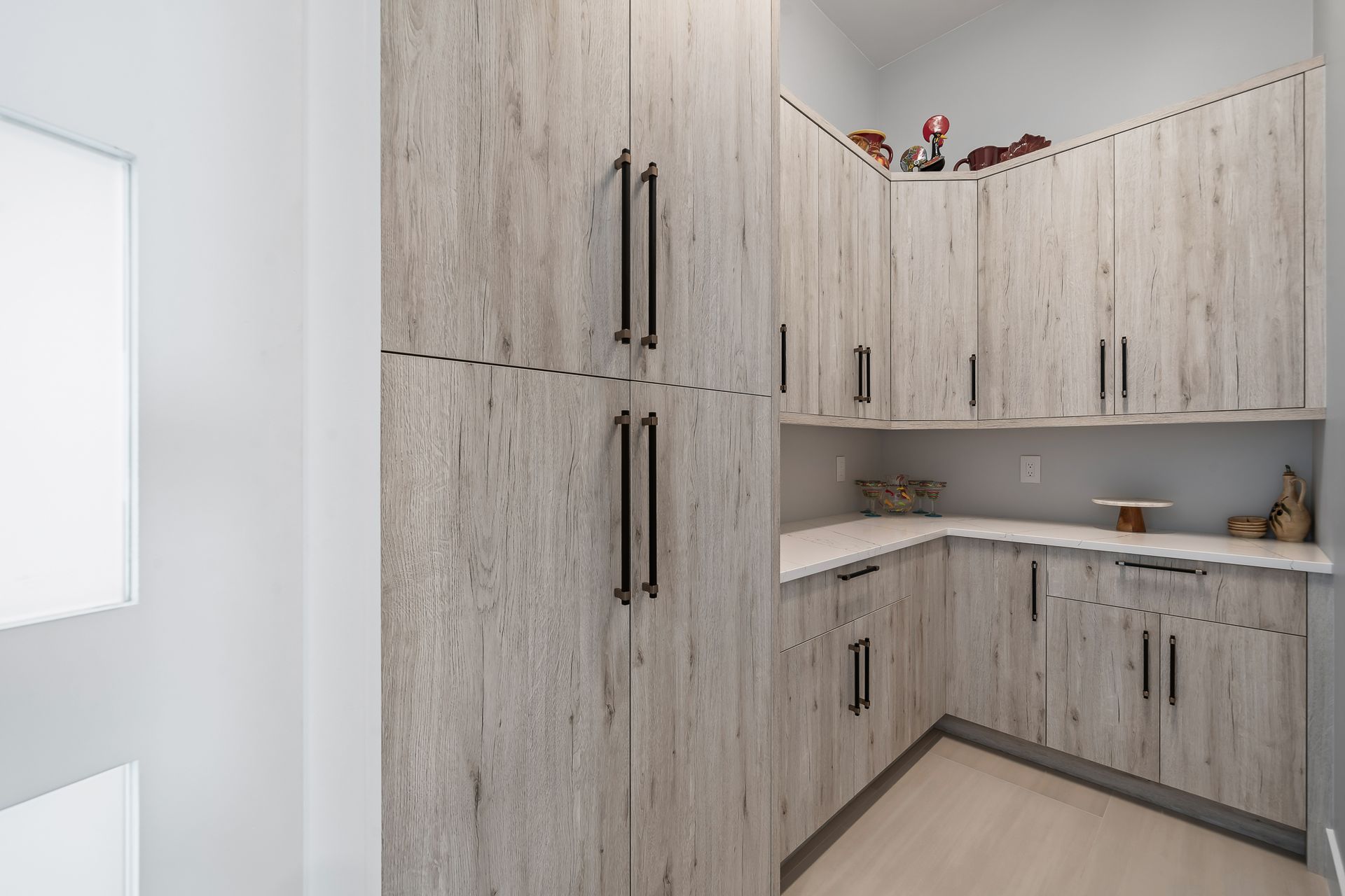 Wooden cabinets in a pantry with a white countertop and dark handles.