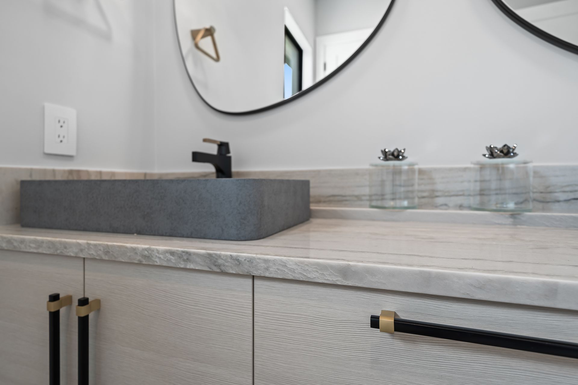 Bathroom vanity with a gray rectangular sink, black faucet, and two oval mirrors.