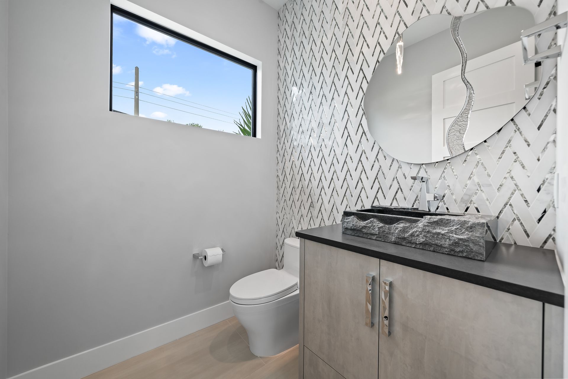 Powder room with patterned accent wall, round mirror, floating vanity, and a window.
