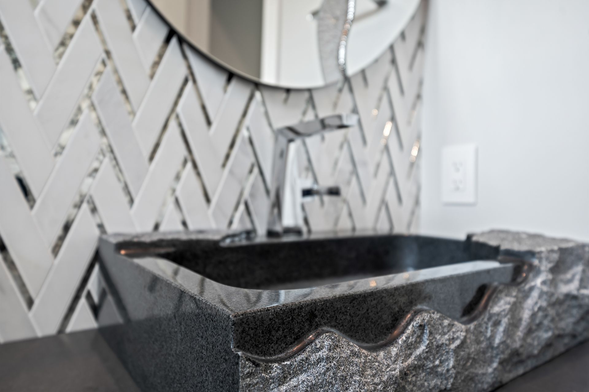 Black granite sink with textured edge, chrome faucet, and herringbone tile backsplash.