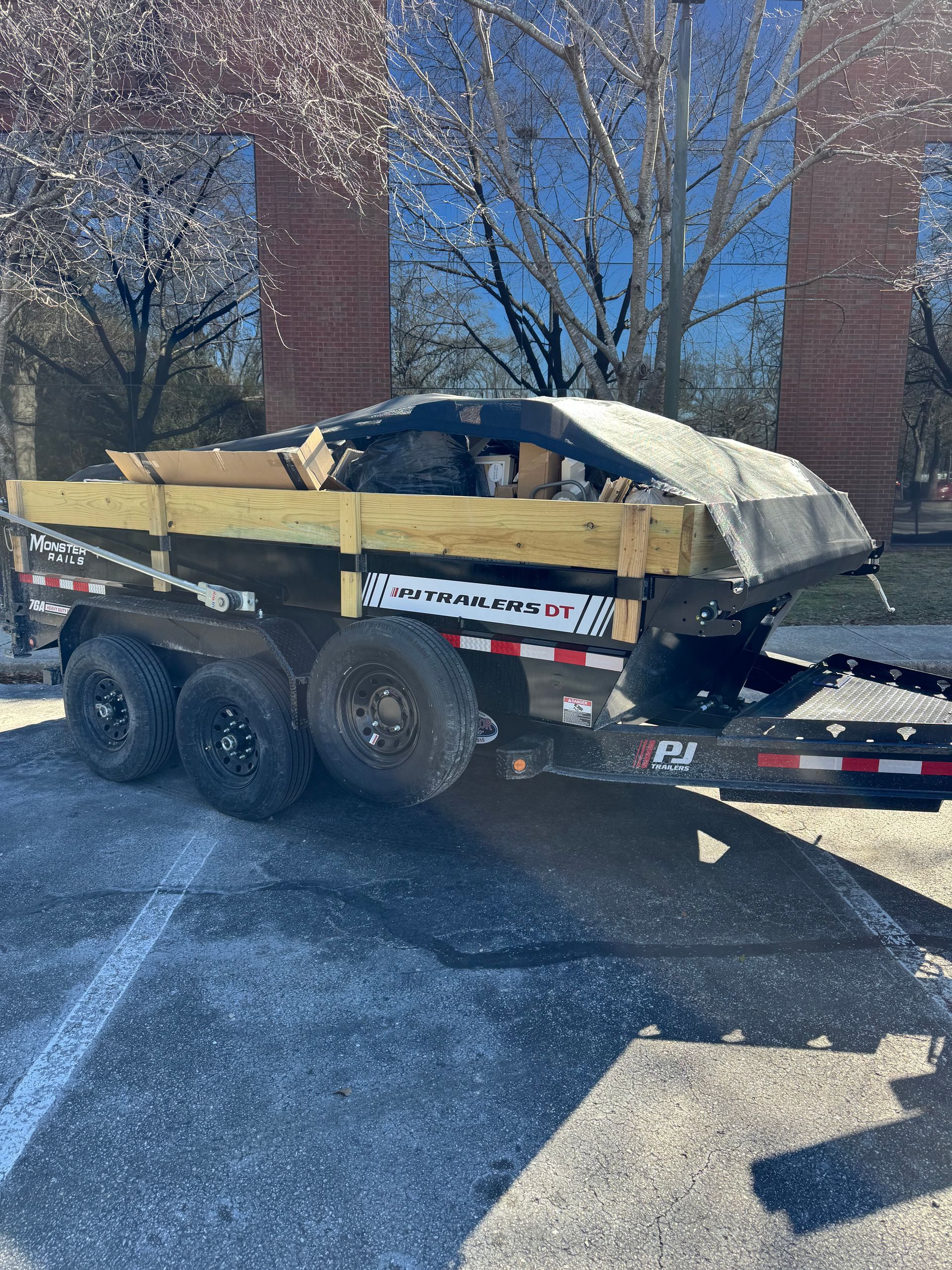 Loaded dump trailer with debris parked beside brick pillars on a sunny day