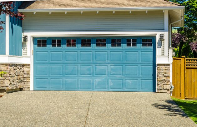 Blue double garage door on a house with a gravel driveway and yellow fence beside it